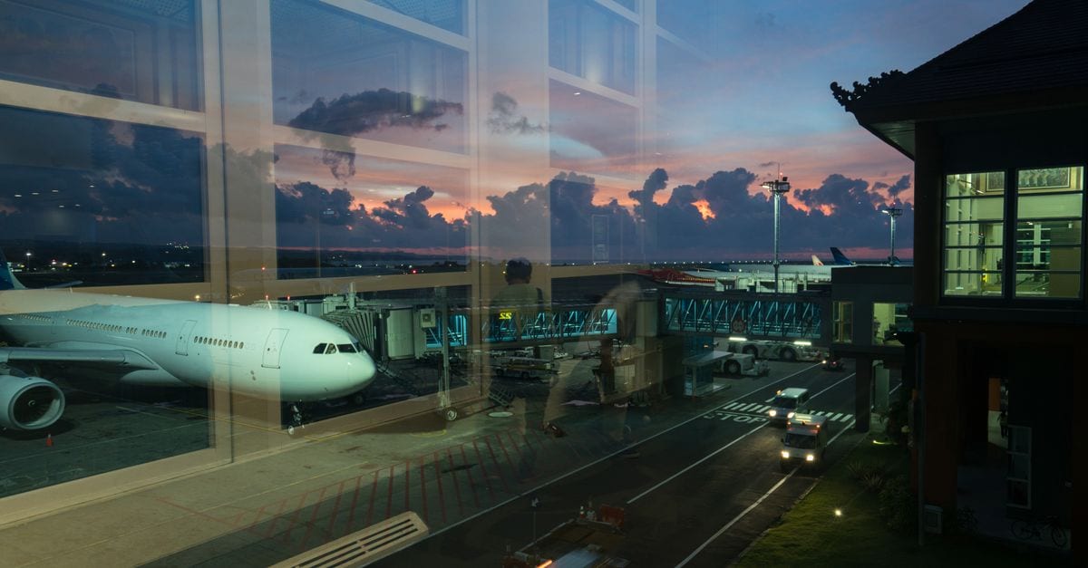Through glass modern aircraft parked near airbridge in contemporary airport against picturesque dusk sky