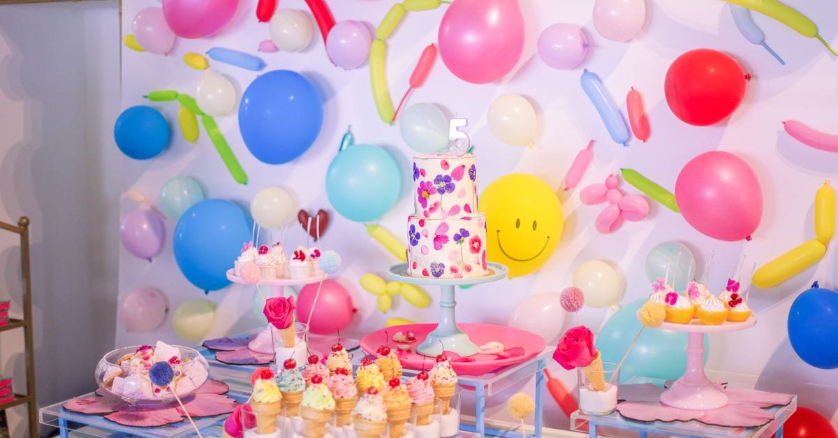 Colorful birthday dessert table with balloons and cake in festive setting.
