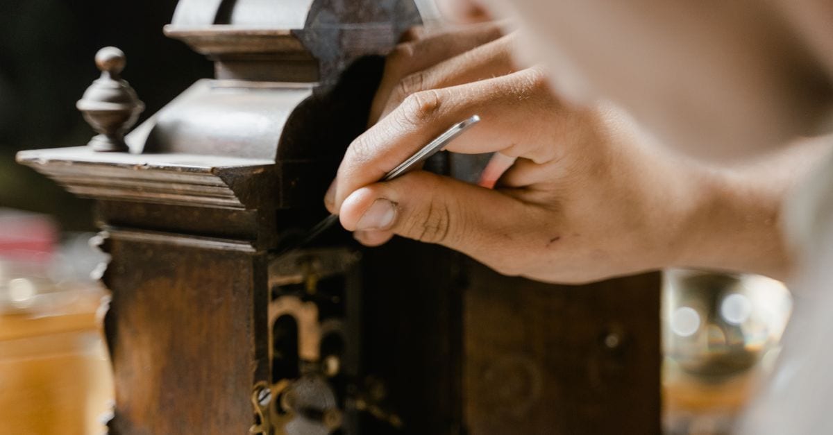 Close-up of hands skillfully restoring an antique wooden clock, highlighting craftsmanship.