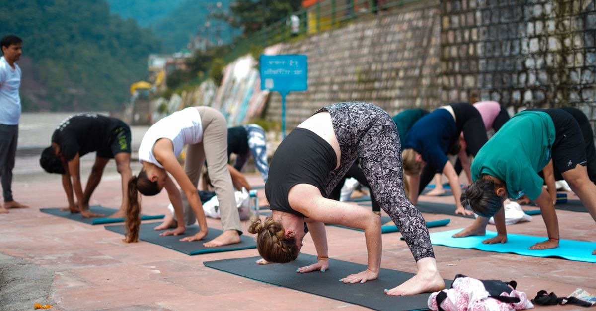 Group practicing yoga outdoors near river with scenic view, promoting wellness and mindfulness