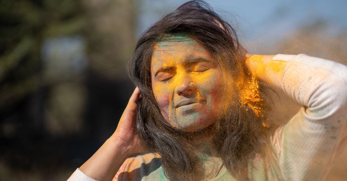 Portrait of woman with closed eyes enjoying Holi colors outdoors.