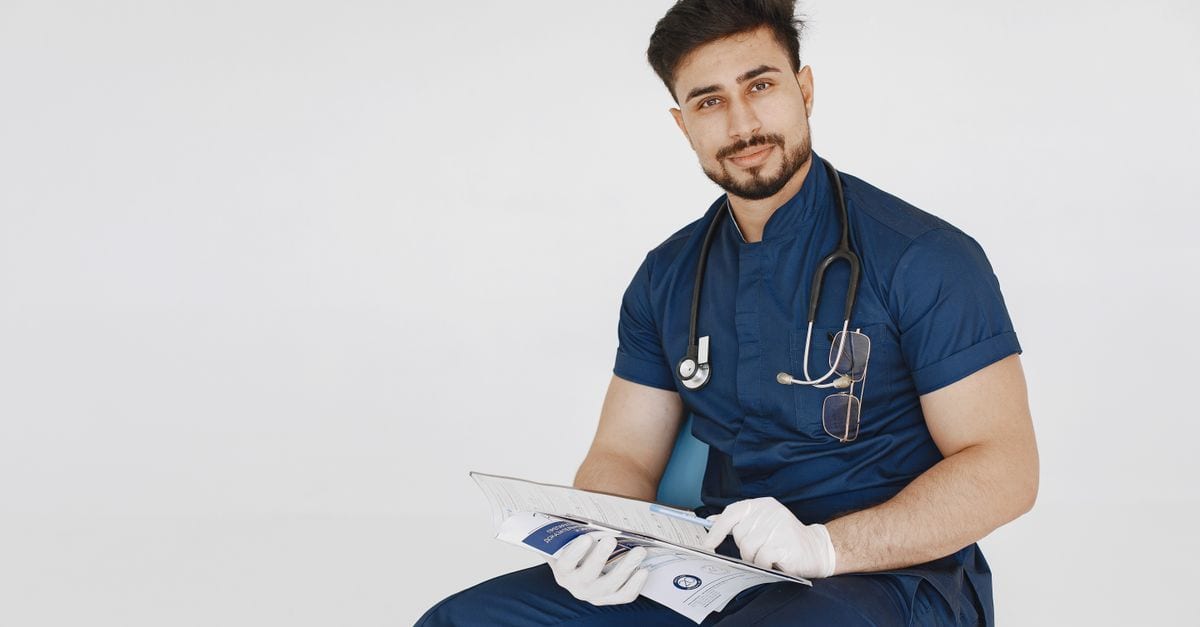Young male doctor in blue scrubs reviewing medical records with a confident smile.