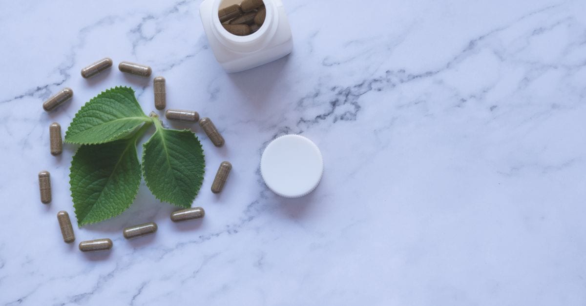 Flat lay of herbal capsules, leaves, and bottle on marble surface, symbolizing natural wellness.