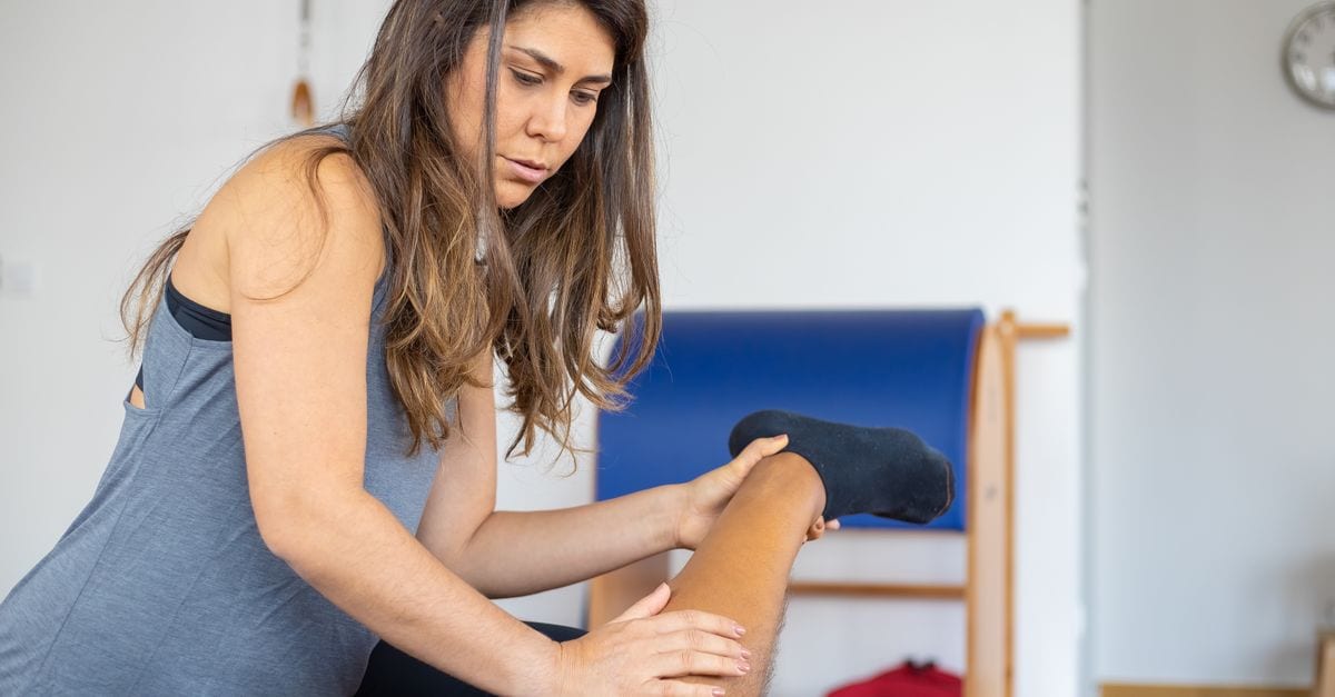 A female trainer assists a client with leg stretching indoors. Focus on fitness and flexibility training.
