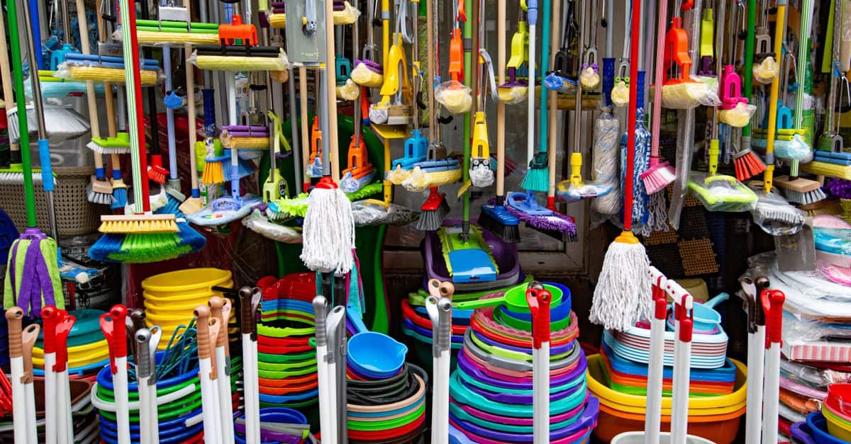 Various colorful mops and brushes arranged with stack of plastic basins and bins in household goods supermarket