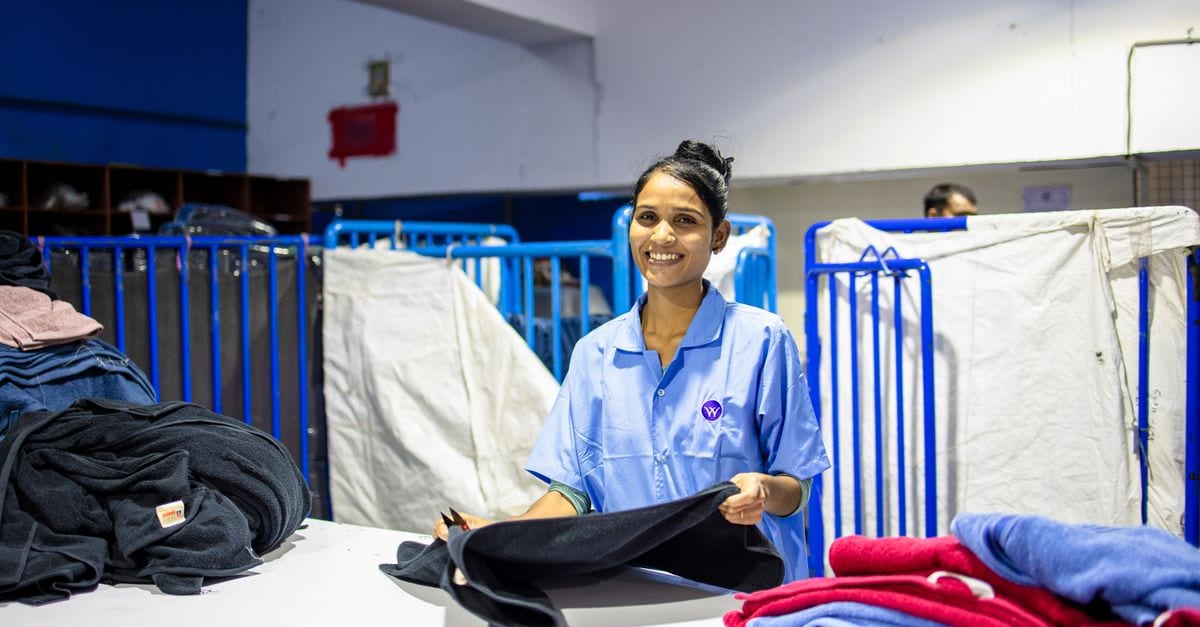 A smiling female textile worker folding clothes inside a factory setting, showcasing the blue-collar work environment.