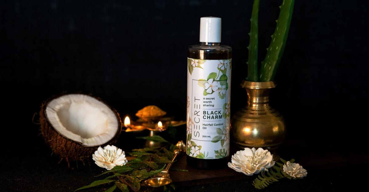 Stylish presentation of herbal hair oil with coconut and aloe on a black background.