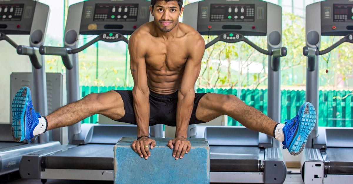 Shirtless muscular man performing calisthenics in an indoor gym in Chandigarh, India.