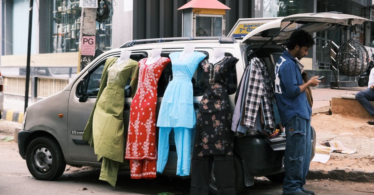 Outdoor street market in Bengaluru with clothes displayed on a car, man using phone nearby.